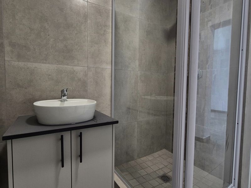 Modern bathroom featuring a vessel sink on a vanity cabinet and a glass-enclosed shower with neutral grey wall and floor tiling.
