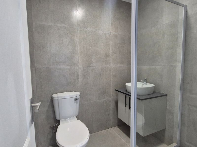 Modern bathroom featuring grey tiled walls, a floating vanity with a vessel sink, a toilet, and a glass-enclosed shower.