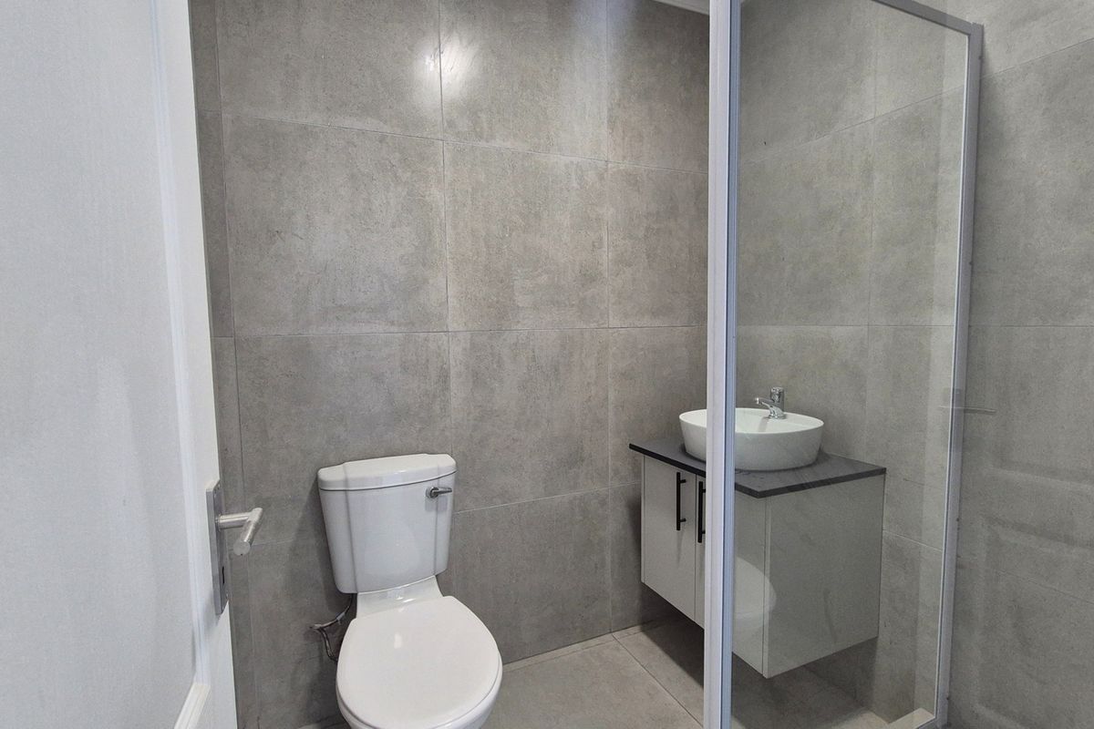 Modern bathroom featuring grey tiled walls, a floating vanity with a vessel sink, a toilet, and a glass-enclosed shower.