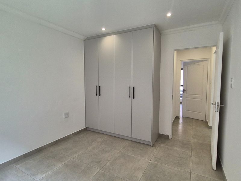 A clean, modern bedroom featuring neutral tiled flooring, built-in cupboards with contemporary hardware, and recessed ceiling lighting.