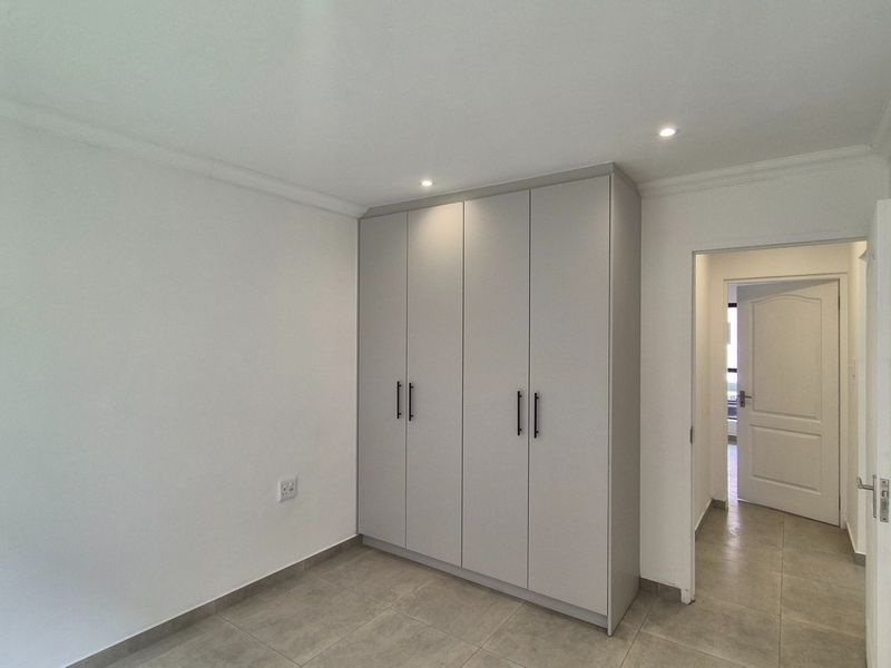 A clean, modern bedroom featuring neutral tiled flooring, recessed downlighting, and ample built-in cupboard storage.