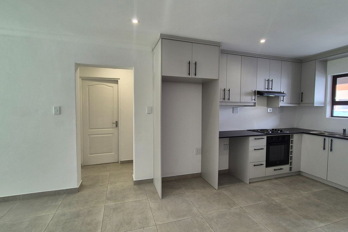 Modern kitchen featuring light grey cabinetry, dark countertops, built-in oven, gas hob, and tiled flooring in an open-plan layout.