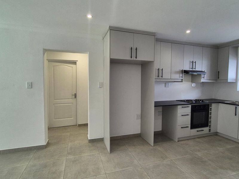 Modern kitchen featuring light grey cabinetry, dark countertops, built-in oven, gas hob, and tiled flooring in an open-plan layout.