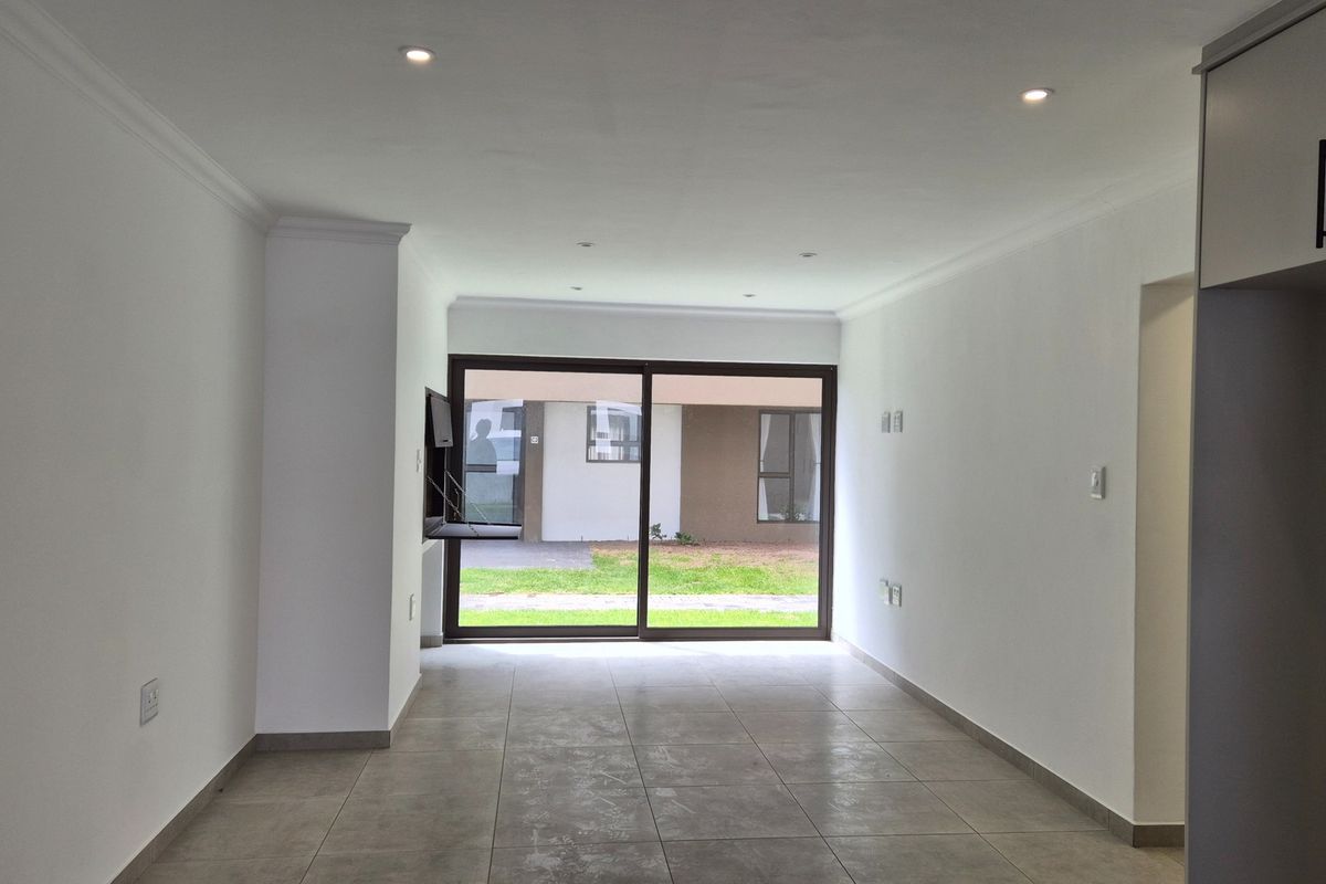 An open-plan living area featuring neutral tiled flooring, recessed downlights, and a large sliding glass door providing access to the exterior.