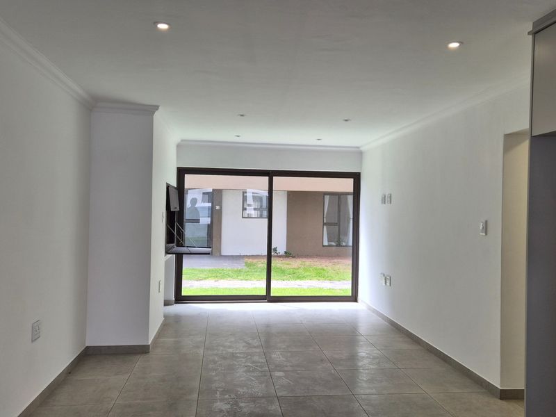 An open-plan living area featuring neutral tiled flooring, recessed downlights, and a large sliding glass door providing access to the exterior.