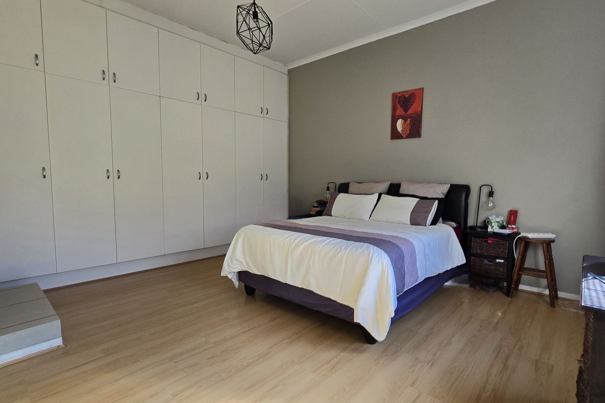 A spacious bedroom featuring extensive floor-to-ceiling built-in cupboards, light-toned laminate flooring, and a neutral wall finish.