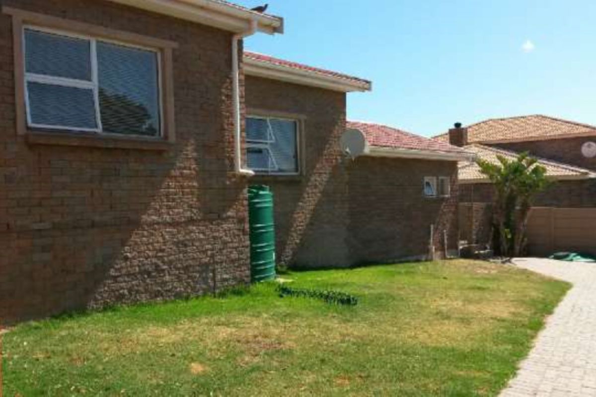 Rear view of the property featuring a face brick facade, tiled roof, paved driveway, and a rainwater tank set within a private garden area.