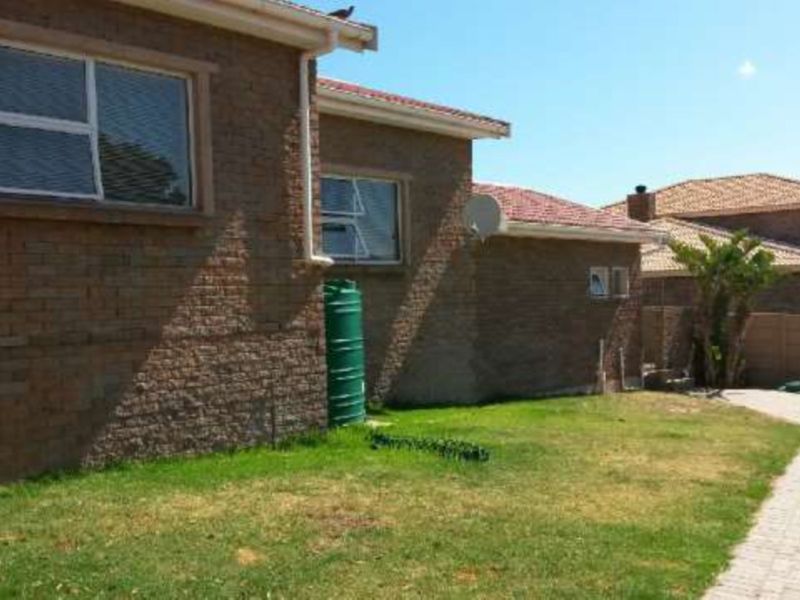 Rear view of the property featuring a face brick facade, tiled roof, paved driveway, and a rainwater tank set within a private garden area.