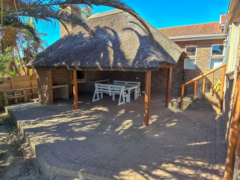 Covered outdoor patio area featuring a traditional thatched roof, built-in brick braai, and paved flooring, ideal for outdoor entertaining.