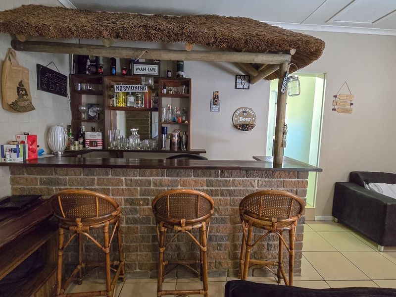 A dedicated indoor bar area featuring a built-in brick counter with a rustic thatched roof canopy and integrated shelving.