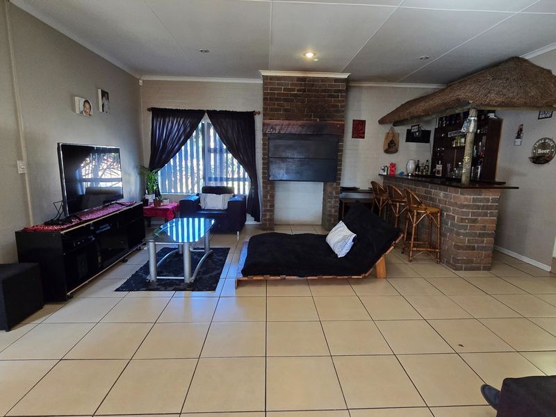 Spacious living area featuring a brick fireplace and a built-in bar with a thatch canopy, finished with neutral floor tiles throughout.