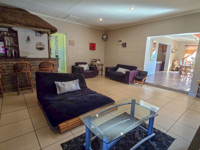 Spacious living area featuring a built-in brick bar with a thatched roof, recessed lighting, and neutral tiled flooring throughout.