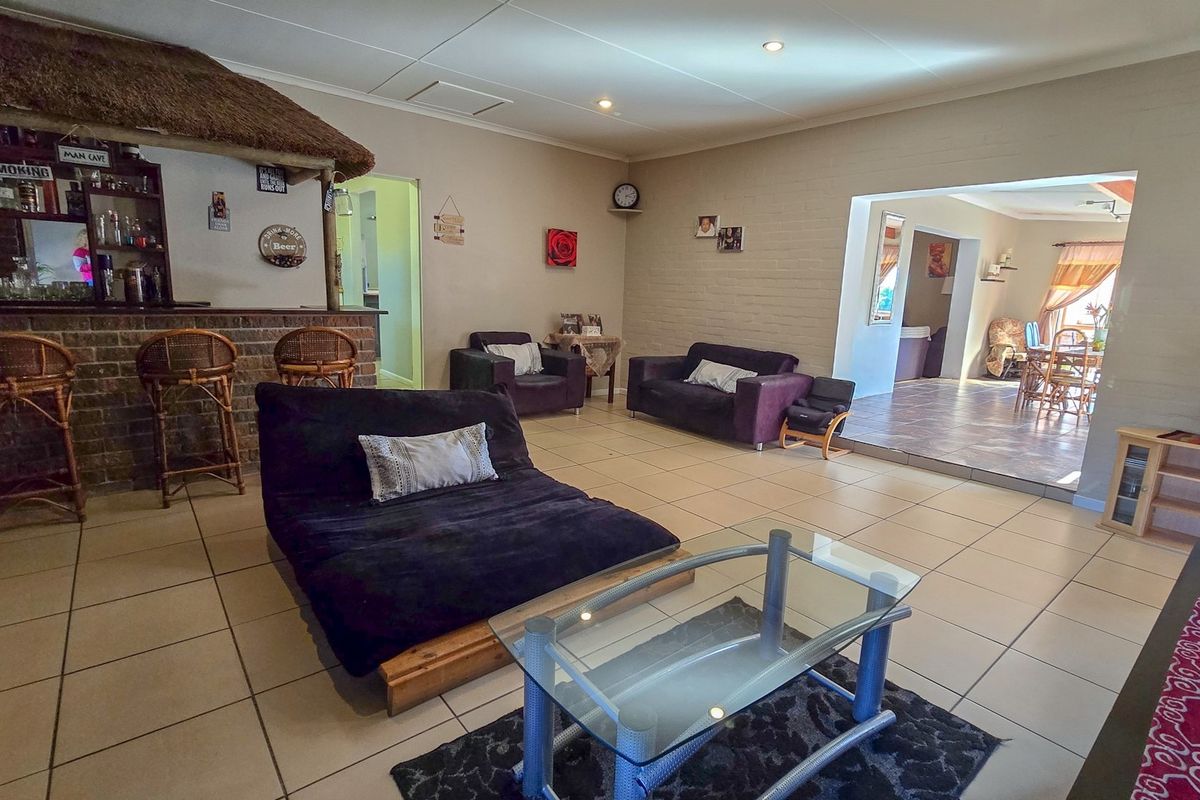 Spacious living area featuring a built-in brick bar with a thatched roof, recessed lighting, and neutral tiled flooring throughout.
