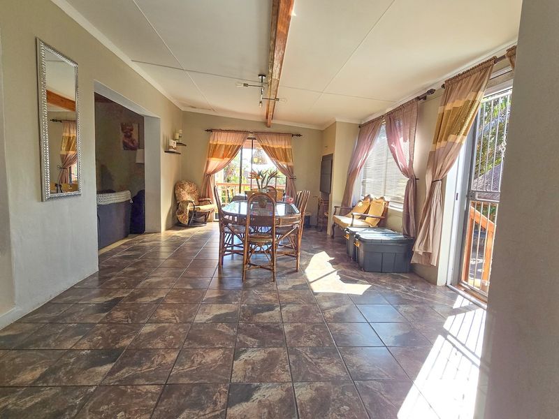 Spacious open-plan living and dining area featuring tiled flooring, an exposed timber ceiling beam, and large sliding glass doors providing natural light.