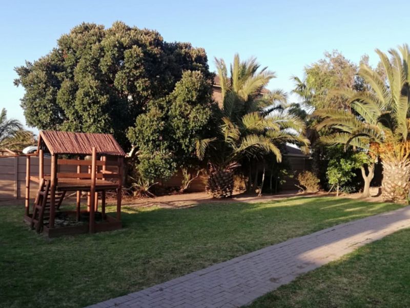 A well-maintained garden featuring a paved walkway, mature trees, and established palm trees, providing a private outdoor space.