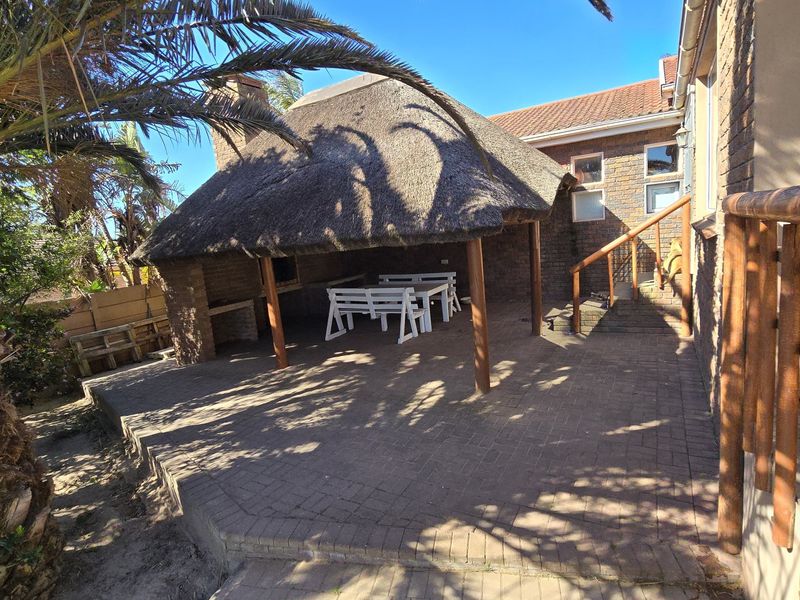 Covered outdoor patio area featuring a traditional thatched roof, built-in braai, and brick paving, providing a functional space for outdoor entertaining.