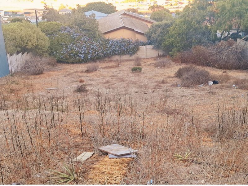A view of a vacant residential plot featuring dry, overgrown vegetation and existing boundary walls, suitable for future development.