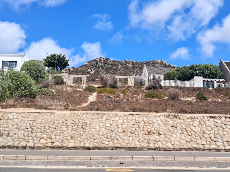 A vacant residential plot featuring a stone retaining wall, concrete boundary pillars, and established fencing, set against a natural rocky hillside backdrop.