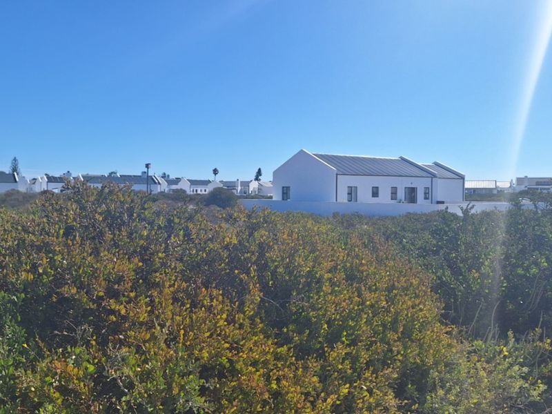 A view of a residential property featuring a white exterior facade and pitched roof, situated within a coastal landscape with native vegetation.