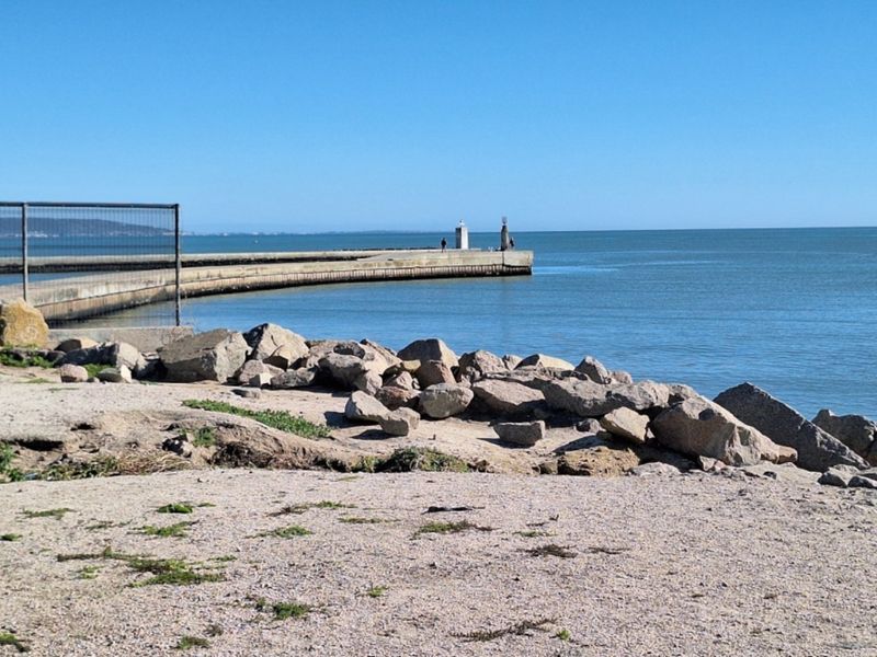 A scenic view of a coastal pier extending into the ocean, featuring a rocky shoreline and protective wire fencing.
