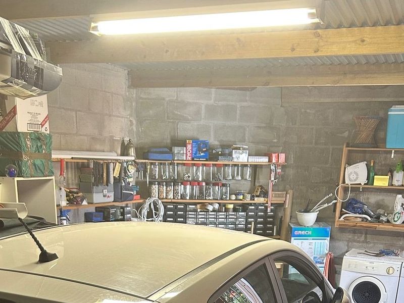 Functional garage space featuring exposed concrete block walls, timber ceiling beams, and integrated laundry plumbing connections.