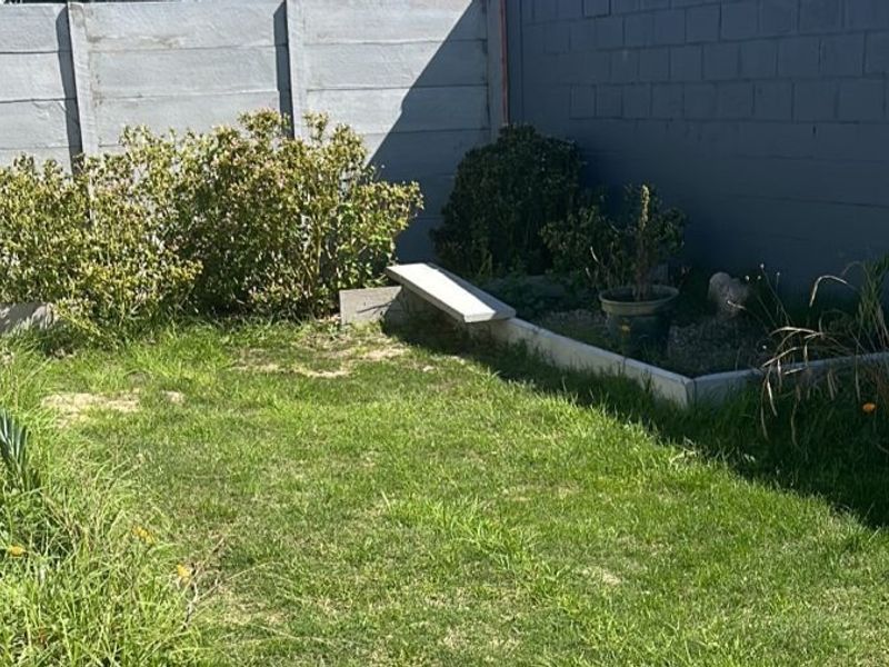 A small backyard garden area featuring a raised planter bed, enclosed by precast concrete and painted masonry boundary walls.