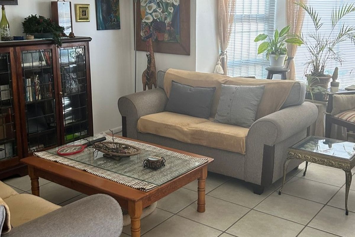 A comfortable living room featuring neutral tiled flooring and large windows fitted with venetian blinds, providing a bright and functional space.