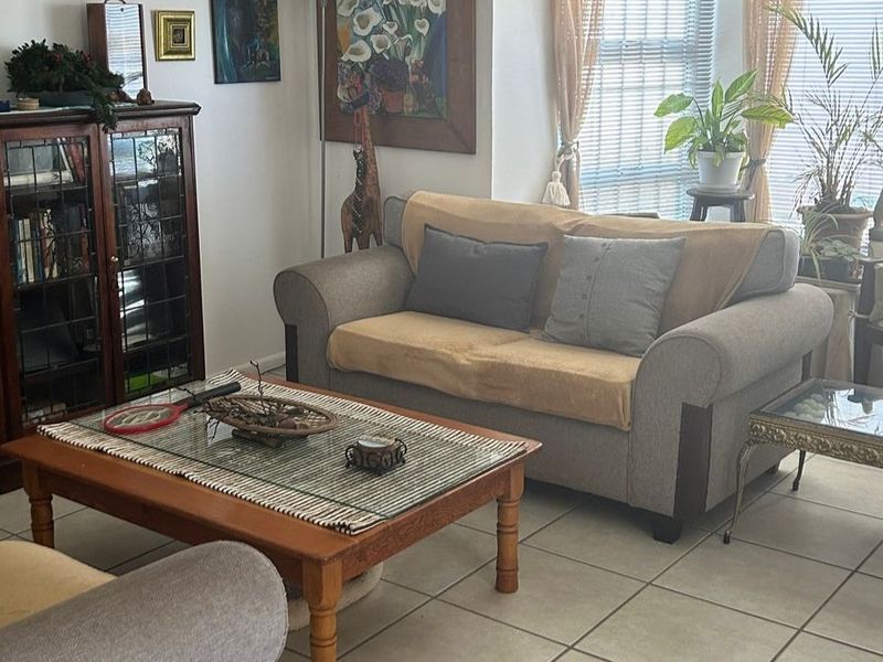 A comfortable living room featuring neutral tiled flooring and large windows fitted with venetian blinds, providing a bright and functional space.