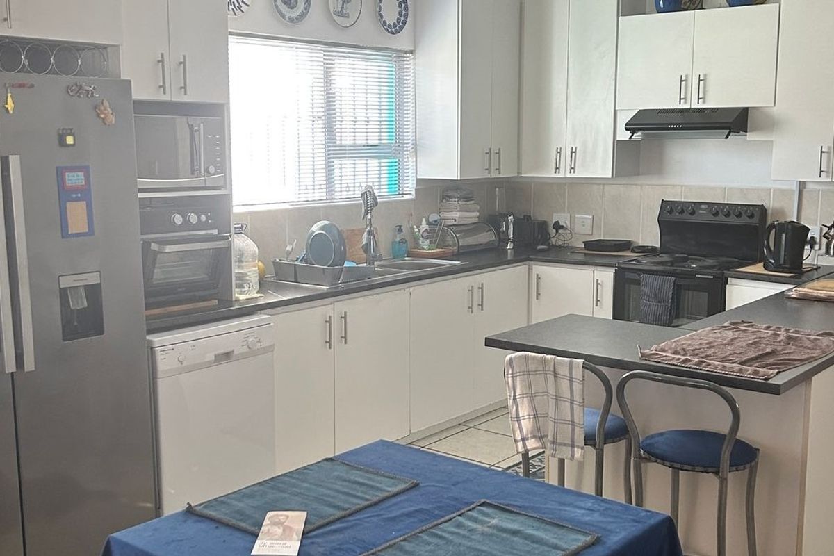 A functional kitchen featuring white cabinetry, dark laminate countertops, a tiled backsplash, and built-in cooking appliances with a breakfast bar area.