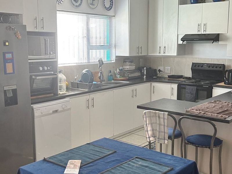 A functional kitchen featuring white cabinetry, dark laminate countertops, a tiled backsplash, and built-in cooking appliances with a breakfast bar area.