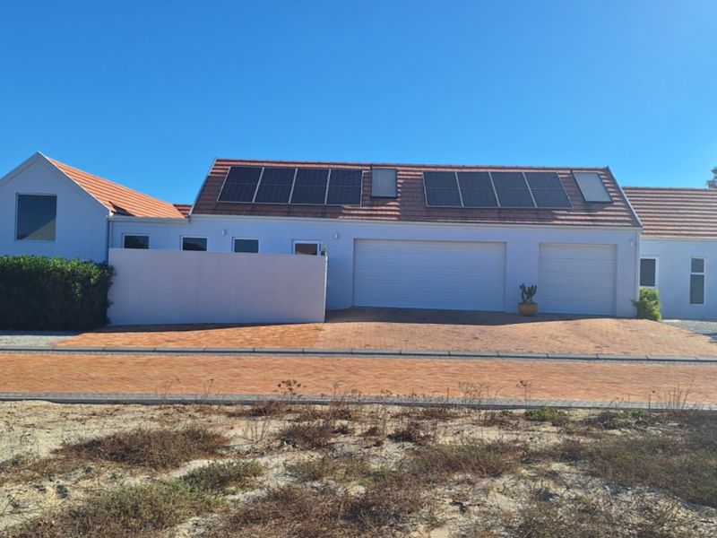 Front elevation of a residential property featuring a double garage, paved driveway, and roof-mounted solar panels under a clear sky.