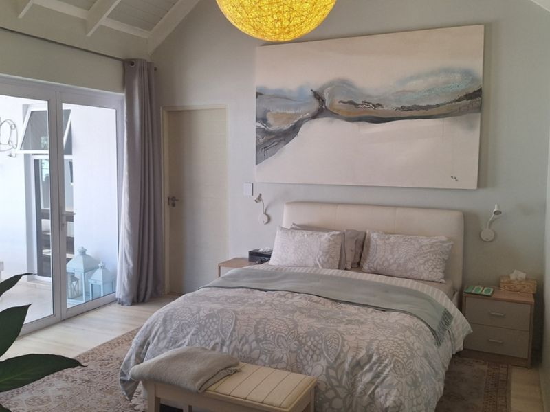 A bright and airy bedroom featuring a vaulted ceiling, neutral finishes, and a sliding glass door providing direct access to an outdoor patio area.