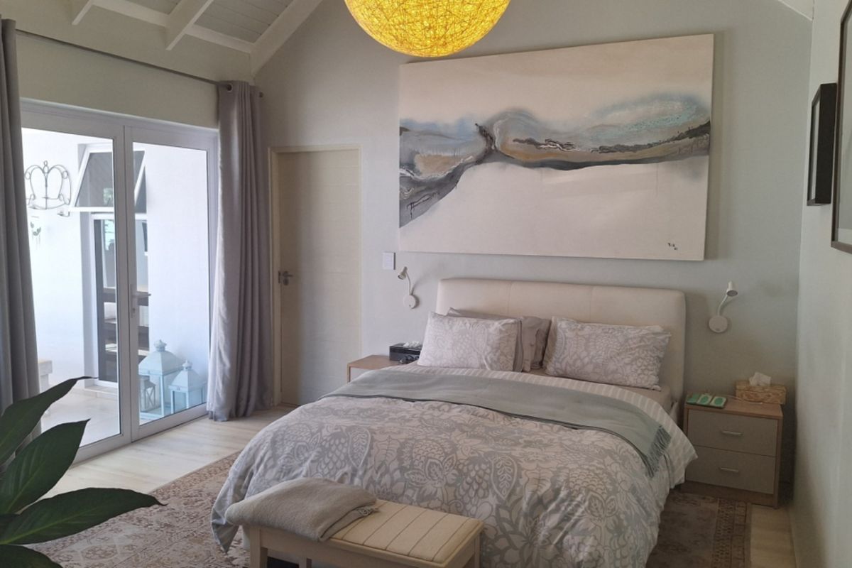 A bright and airy bedroom featuring a vaulted ceiling, neutral finishes, and a sliding glass door providing direct access to an outdoor patio area.