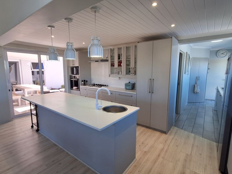Modern kitchen featuring a central island, built-in cabinetry, gas hob, and integrated appliances, with light timber-look flooring and direct access to an outdoor patio area.