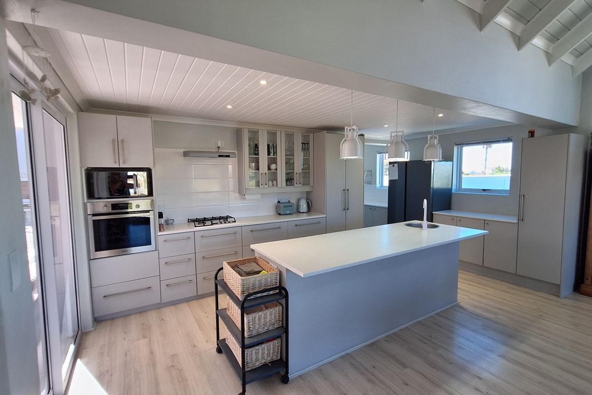 Modern kitchen featuring a central island with sink, built-in oven and microwave, gas hob, and light-toned cabinetry under a vaulted timber ceiling.