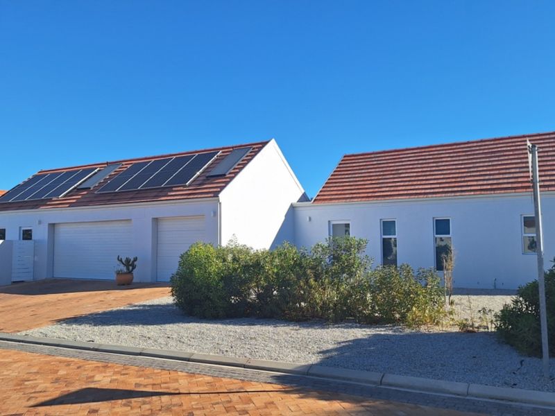 Front exterior view of a modern house featuring a double garage, tiled roof with solar panels, and a paved driveway.