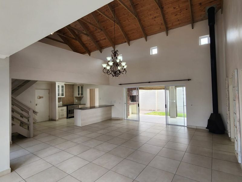 Spacious open-plan living area featuring a vaulted timber ceiling, tiled floors, a modern fireplace, and seamless flow to the outdoor patio.