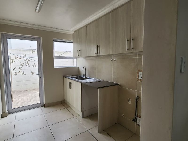 A functional laundry room featuring built-in cabinetry, a stainless steel sink, tiled flooring, and direct access to an outdoor area.