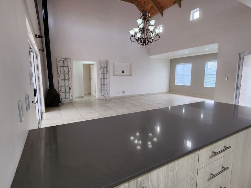 Spacious open-plan living and kitchen area featuring a large island with stone countertops, vaulted ceilings with exposed beams, and a modern freestanding fireplace.