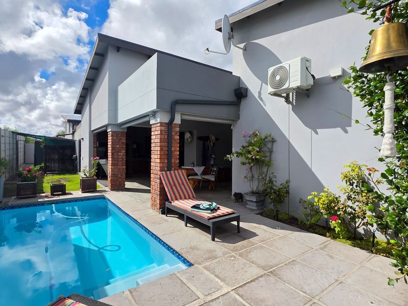 A well-maintained outdoor pool area featuring a paved patio, brick pillars, and a covered patio space, ideal for relaxation and outdoor living.