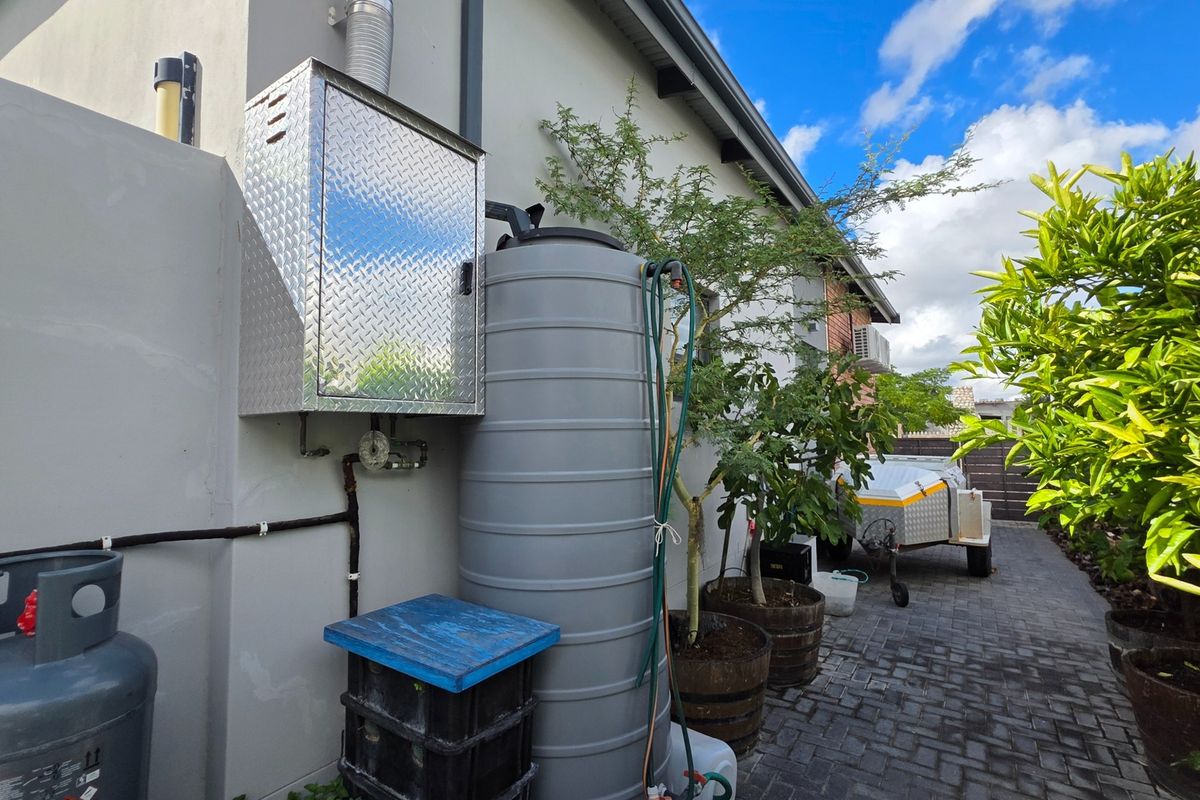 Rear exterior area featuring a water storage tank, gas geyser unit, and paved pathway along the side of the house.