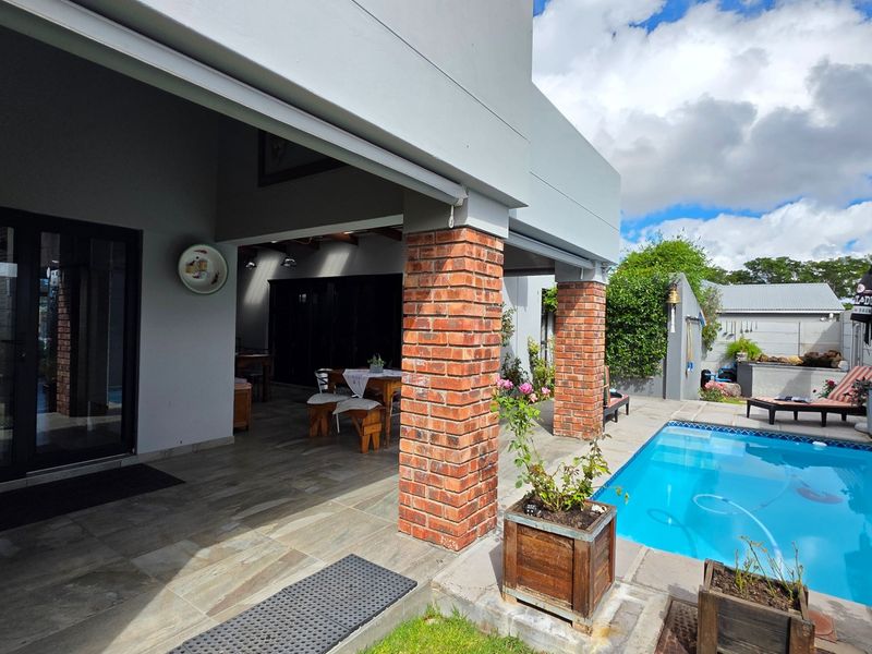 Outdoor entertainment area featuring a tiled patio with brick pillars, a swimming pool, and direct access to the interior through sliding glass doors.
