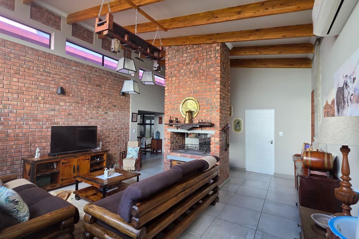 Spacious living room featuring a prominent brick fireplace, exposed timber ceiling beams, tiled flooring, and high-level clerestory windows for natural light.