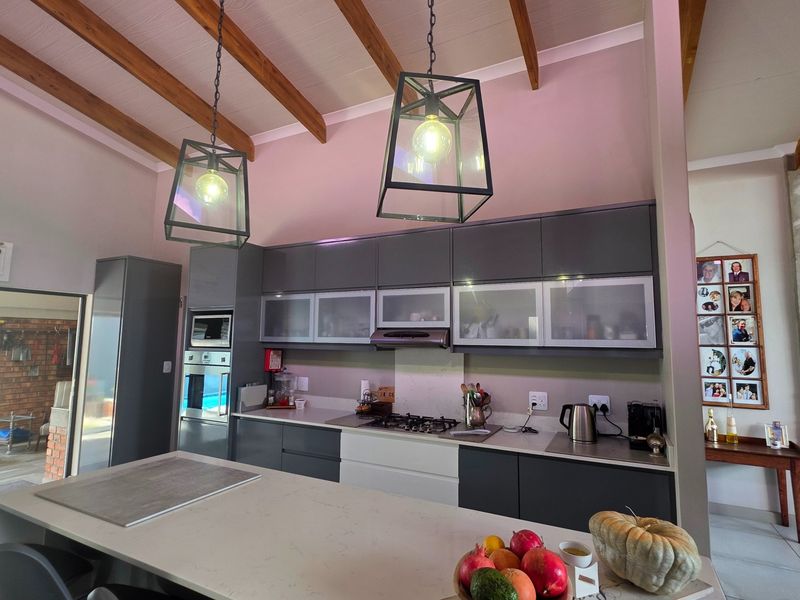 Modern kitchen featuring dark cabinetry, stone island, gas hob, built-in appliances, and striking exposed timber ceiling beams with pendant lighting.