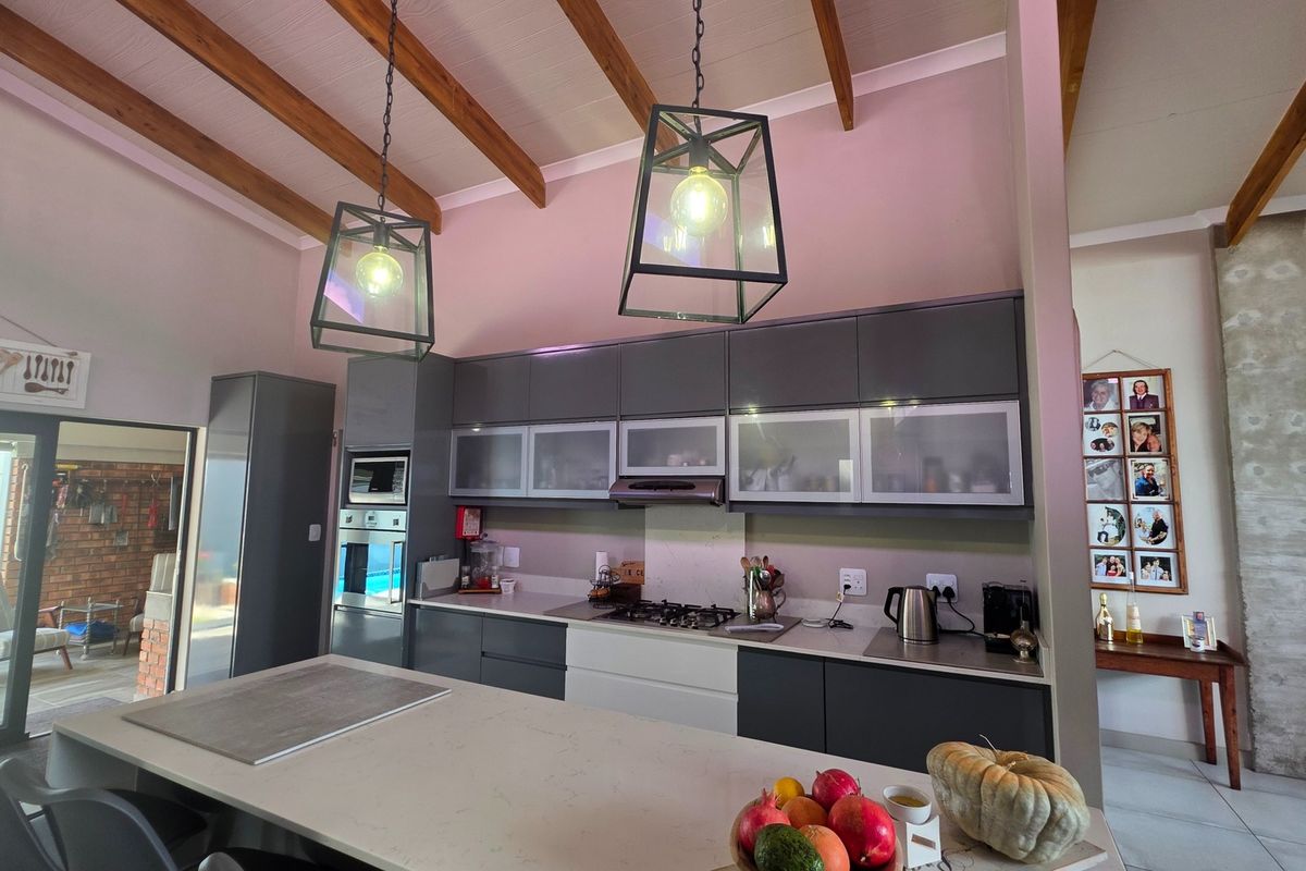 Modern kitchen featuring dark cabinetry, stone island, gas hob, built-in appliances, and striking exposed timber ceiling beams with pendant lighting.