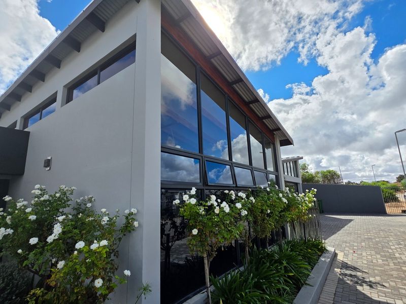 Modern architectural facade featuring extensive glass paneling, a metal roof, and a neatly paved driveway with landscaped garden borders.