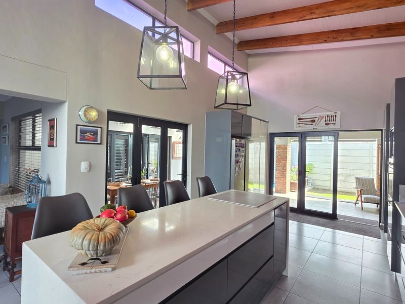 Modern open-plan kitchen featuring a large island with stone countertops, exposed timber beams, and seamless flow to the outdoor patio area.