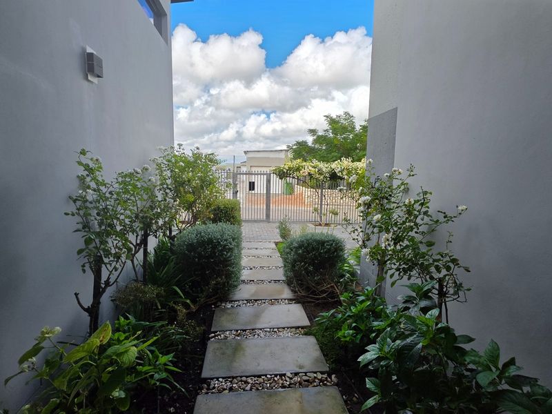 A well-maintained front entrance pathway featuring stone pavers, landscaped garden beds, and a secure metal gate.