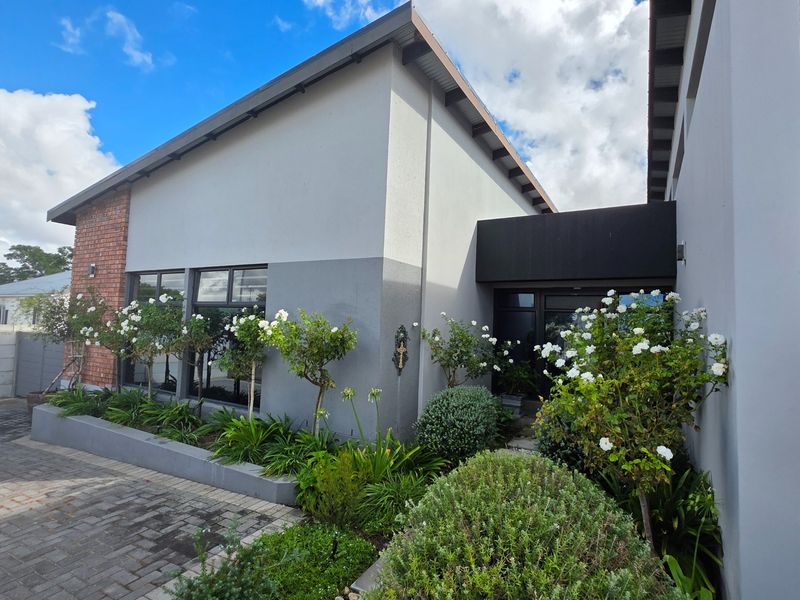 Modern front facade featuring a paved driveway, raised garden beds with established landscaping, and contemporary architectural finishes with aluminium window frames.