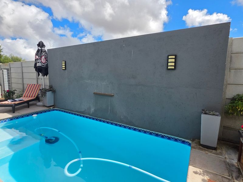 A private swimming pool area featuring a modern grey feature wall with integrated lighting and paved surround.